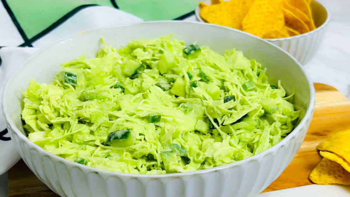 Cabbage salad in a white bowl with chips in the background.