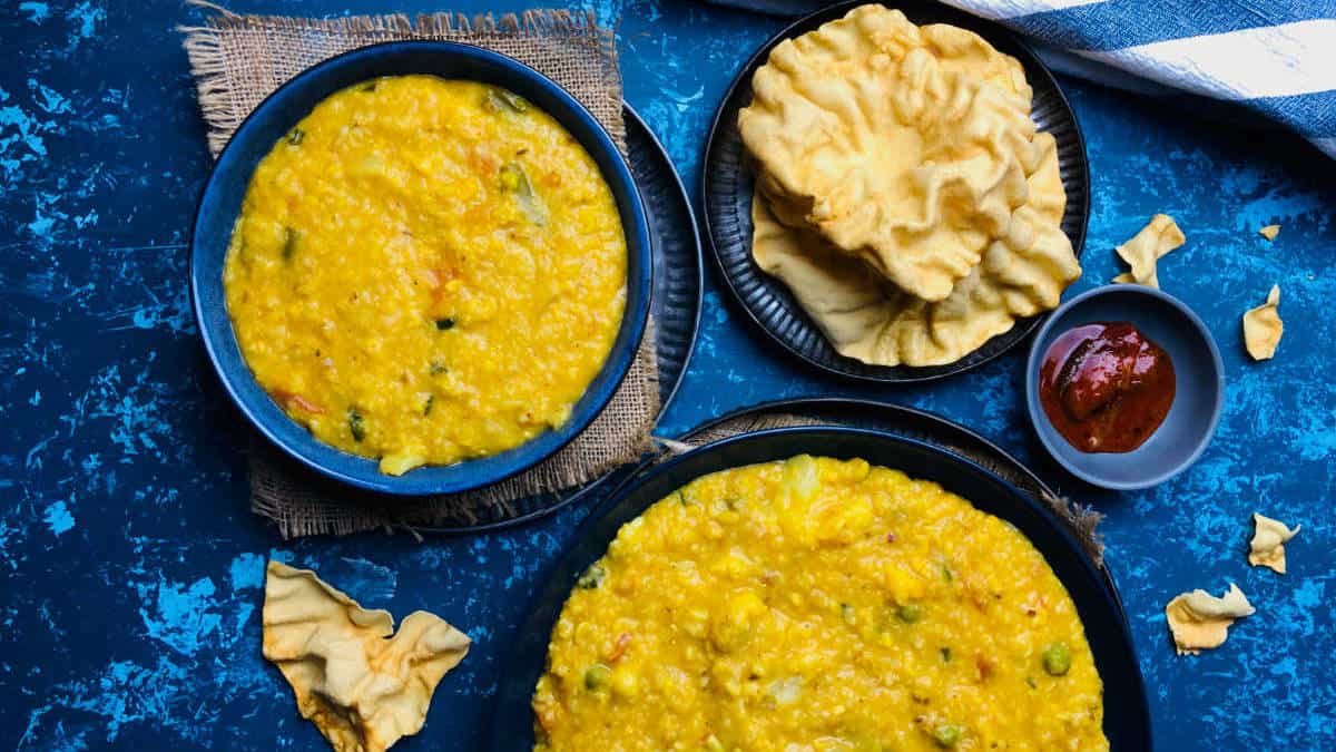 Dalia khichdi in two bowls with papad and pickle in the background.