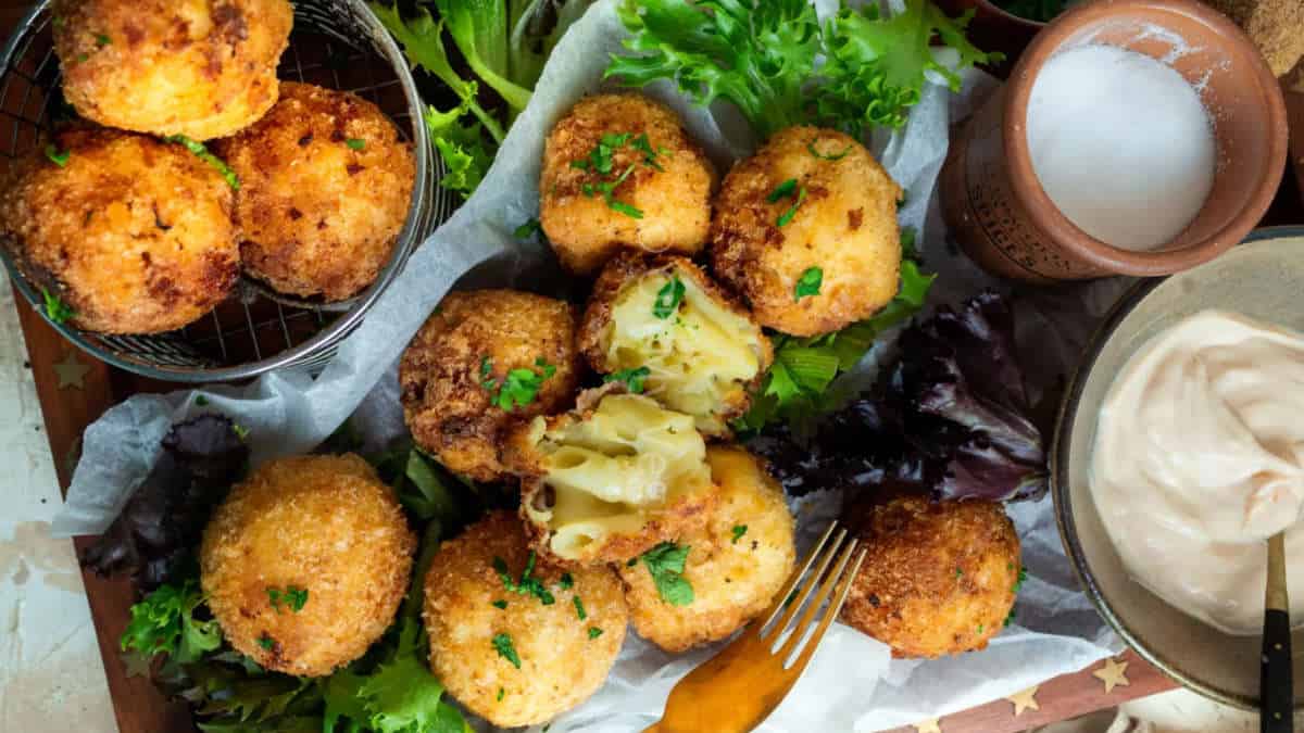 Fried mac and cheese balls on a parchment paper with lettuce in the background.