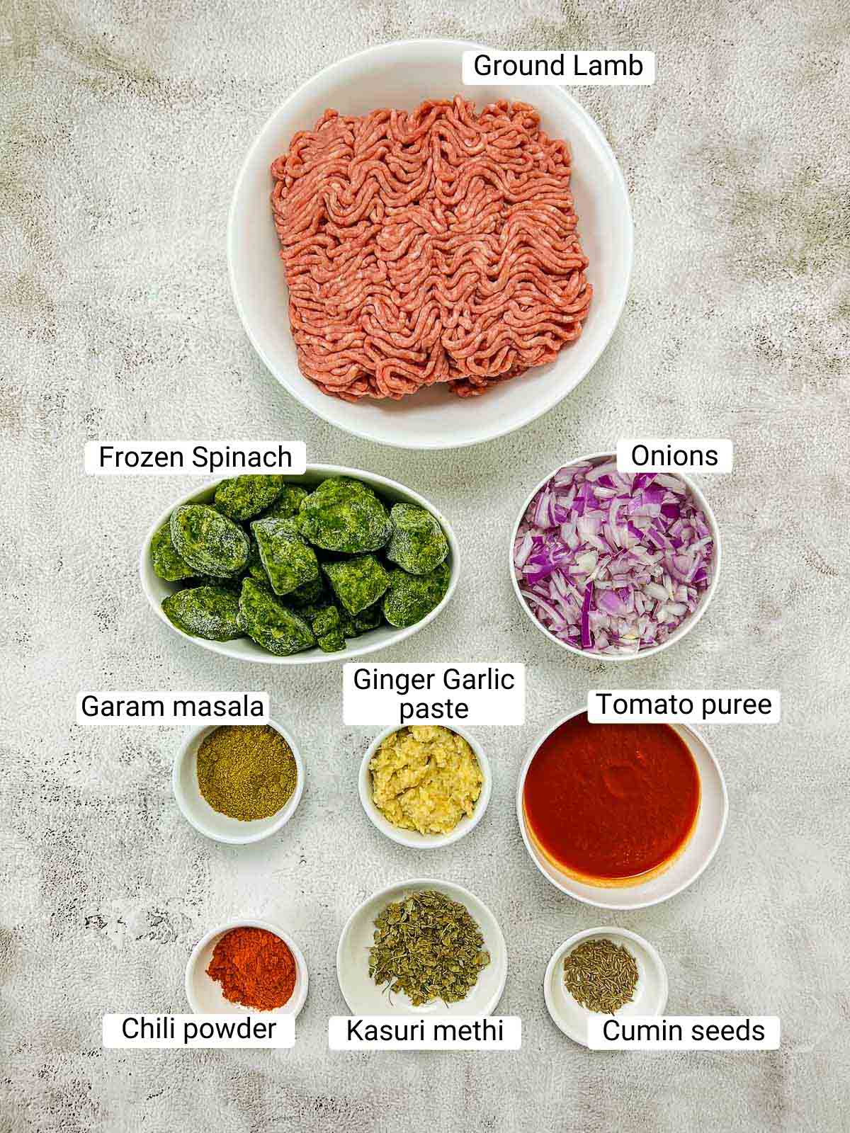 Ingredients to make spinach lamb kofta on a white surface.