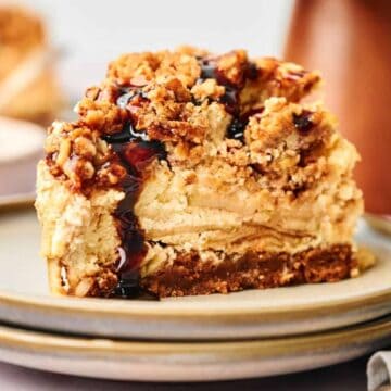 A slice of apple pie stuffed cheesecake on a plate with a spoon.