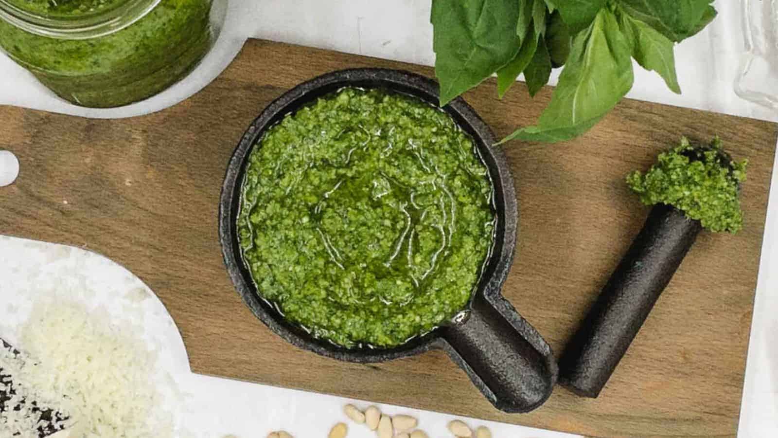 Homemade pesto in a cast iron dish with nuts and basil around it.
