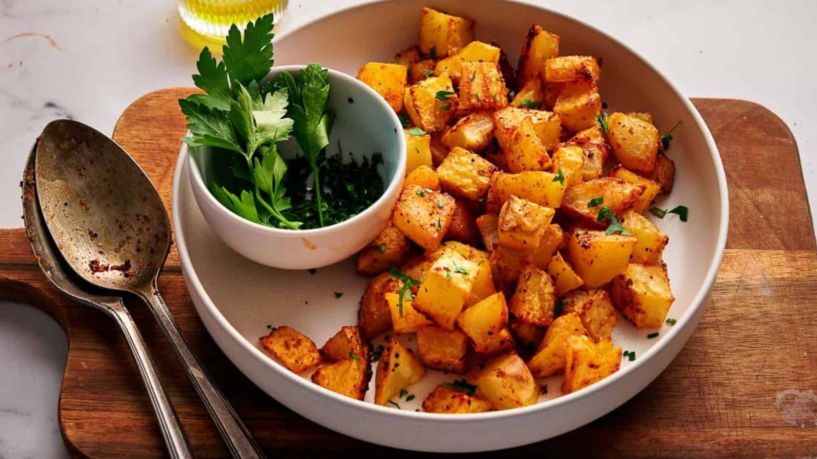 Breakfast potatoes in a serving bowl, with serving spoons and a small bowl of fresh parsley.