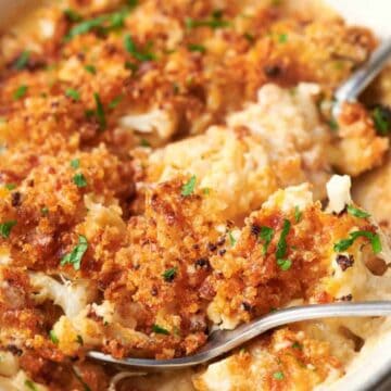 Cheesy cauliflower casserole in a white dish with spoons.