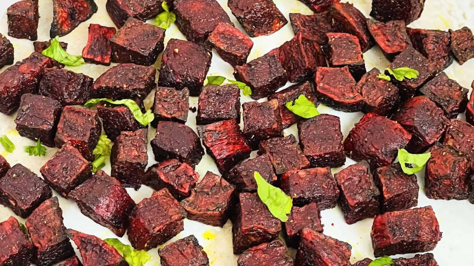 Diced roasted beetroot pieces scattered on a white plate, garnished with green herbs.