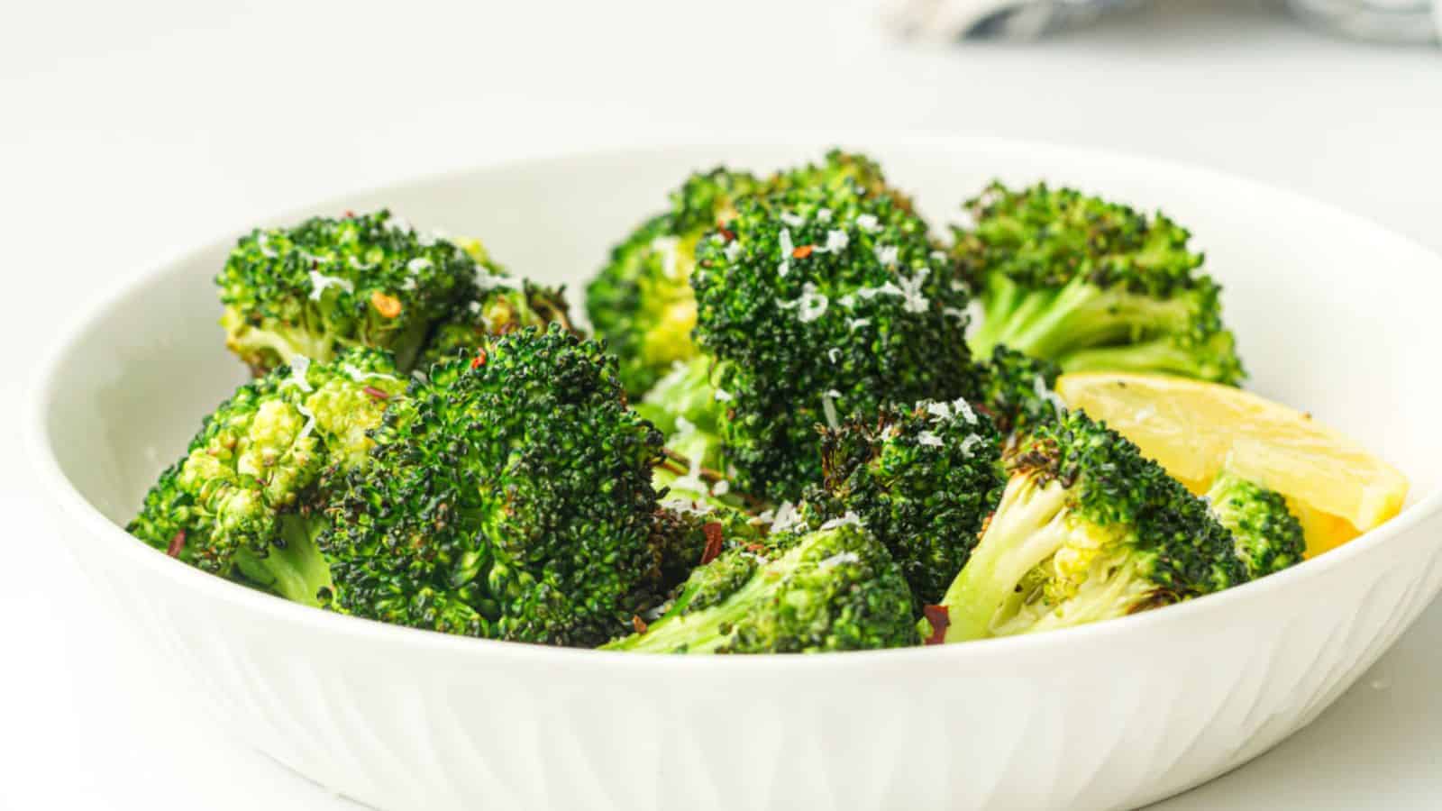 A bowl of air fried broccoli garnished with grated cheese and lemon wedges.