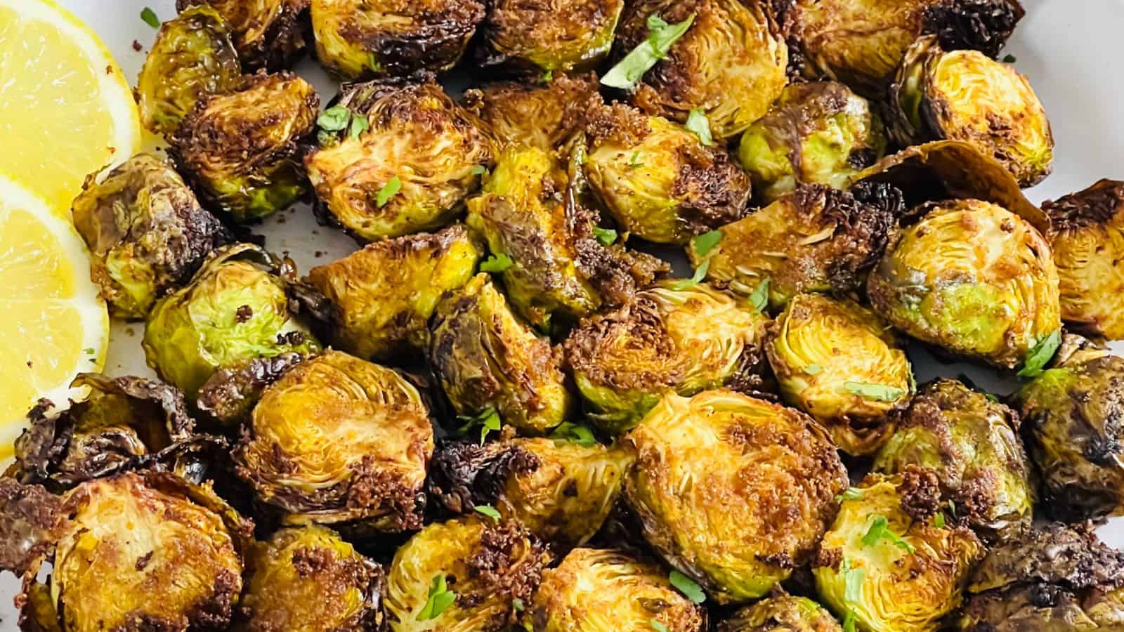 Air Fryer Brussels Sprouts garnished with lemon wedges on a plate.