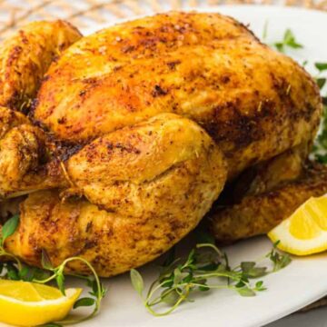 Roasted air fryer whole chicken served on a white plate with lemon wedges.