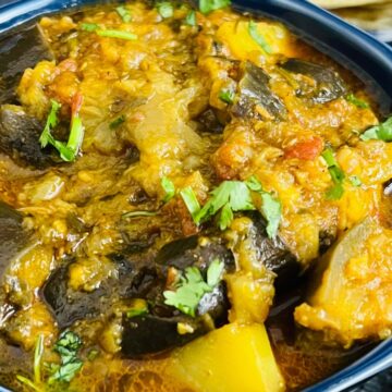 A vibrant bowl of aloo baingan garnished with fresh cilantro, served alongside lime wedges.