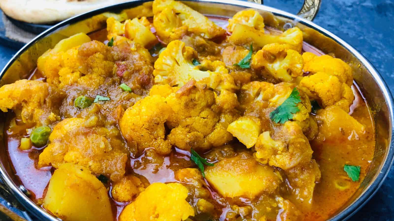 A bowl of cauliflower curry with tomatoes and cucumbers.