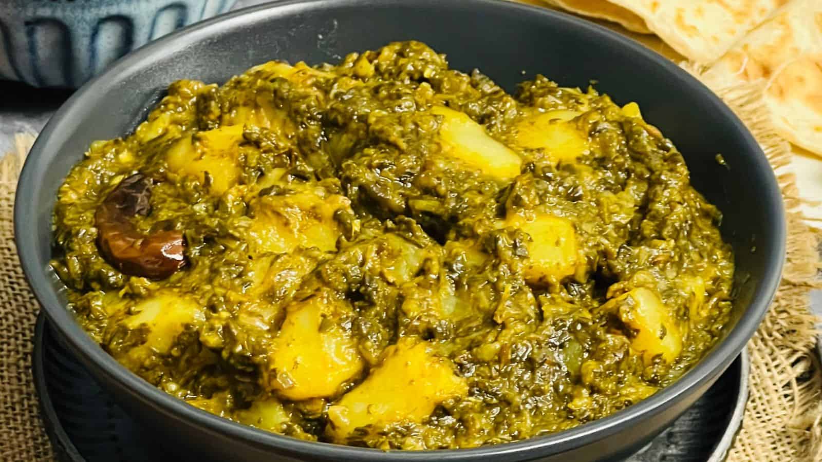 Two bowls of potato and spinach curry on a green cloth.