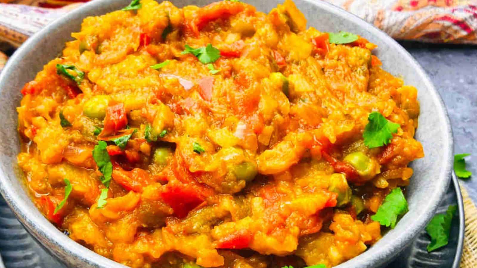 A bowl of baingan bharta, an indian dish made of mashed eggplant mixed with spices, tomatoes, and garnished with cilantro.