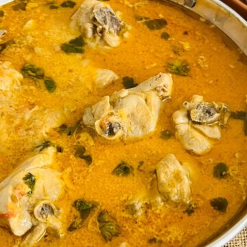 A bowl of traditional chicken curry served with naan bread on the side.