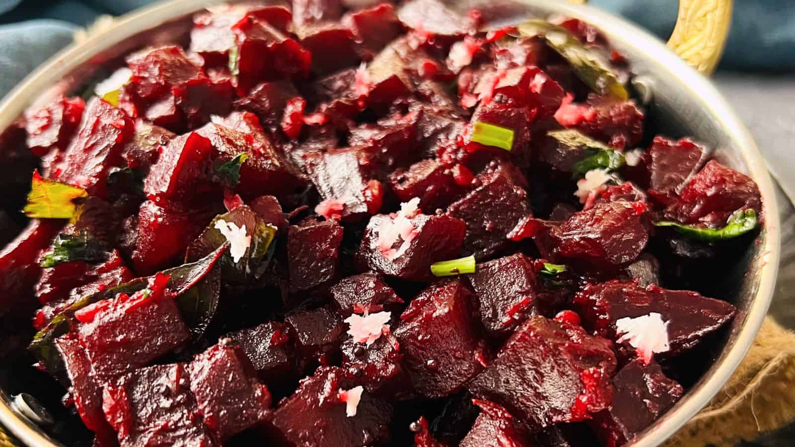 A bowl of diced Beetroot Palya garnished with herbs and sprinkled with salt, served on a dark textured background.