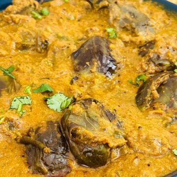 A bowl of eggplant curry garnished with cilantro, accompanied by flatbread.