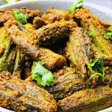 A bowl of spiced and cooked okra garnished with fresh herbs.