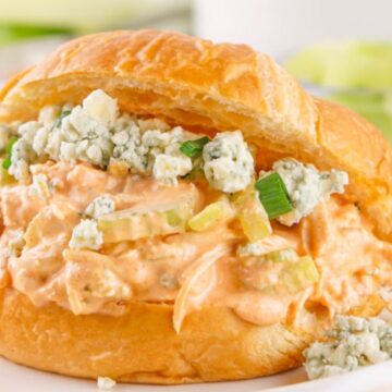A buffalo chicken salad sandwich with blue cheese and celery in a croissant, served on a white plate.