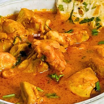 A bowl of chicken curry garnished with herbs, accompanied by a piece of naan bread.