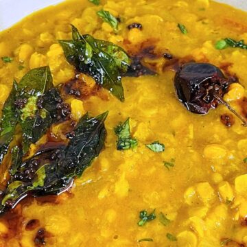 Chana Dal with yellow lentils, garnished with fresh cilantro and tempered spices, including curry leaves and dried chilies.