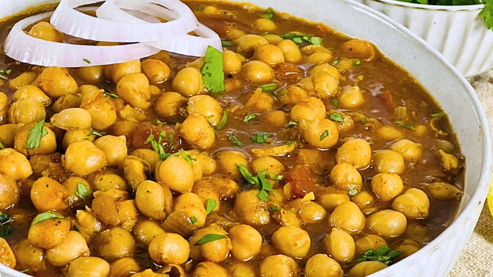 A bowl of Chana Masala garnished with fresh herbs and onion slices.