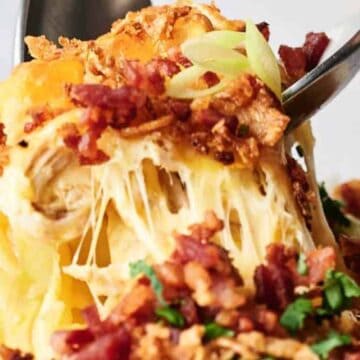A fork lifting a cheesy bite from a bowl of chicken casserole topped with bacon and breadcrumbs.