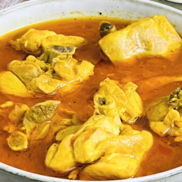 A bowl of Chicken Curry Home Style with pieces of meat and visible spices in a rich, orange sauce.