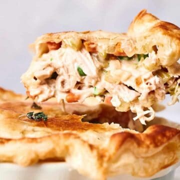 A slice of chicken pot pie being lifted, showing its creamy filling with vegetables, garnished with herbs.