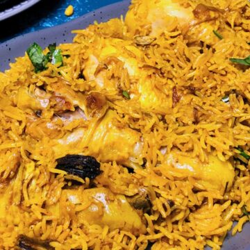 A platter of Chicken Pulao with vibrant yellow rice, herbs, and chicken pieces, served in a blue dish.