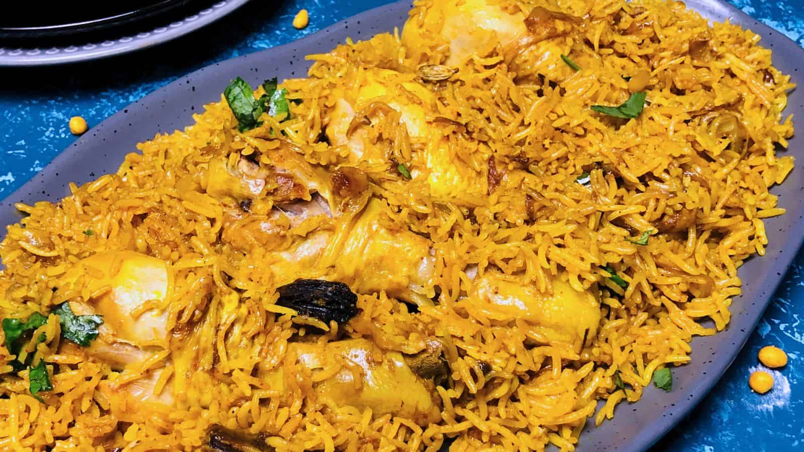 A platter of Chicken Pulao with vibrant yellow rice, herbs, and chicken pieces, served in a blue dish.