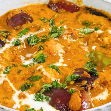 A bowl of creamy chicken tikka masala garnished with fresh herbs, served alongside a dish of rice.