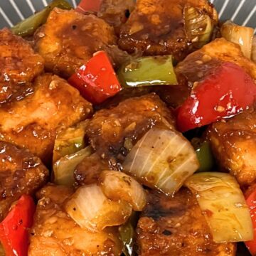 Bowl of Chilli Paneer with red bell peppers and onions in a glossy sauce.
