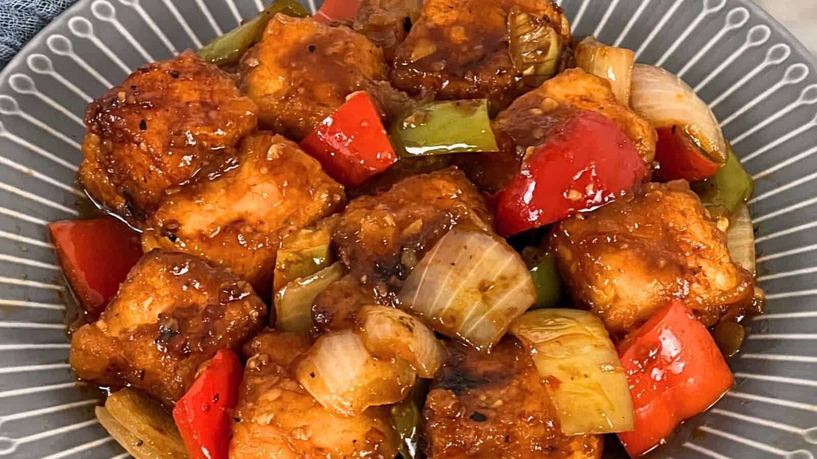 Bowl of Chilli Paneer with red bell peppers and onions in a glossy sauce.