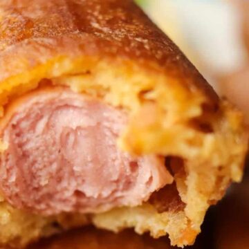 Close-up of a bitten corn dog showing its interior with a layer of crispy fried batter and a hot dog inside.
