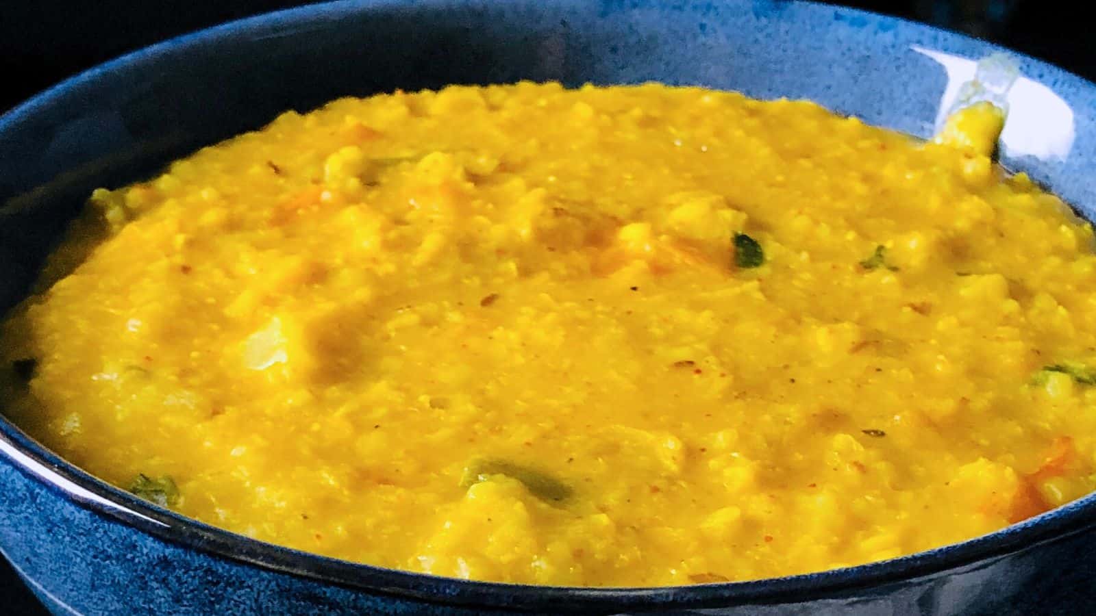 Dalia Khichdi served in a dark blue bowl with visible chunks of vegetables and spices.