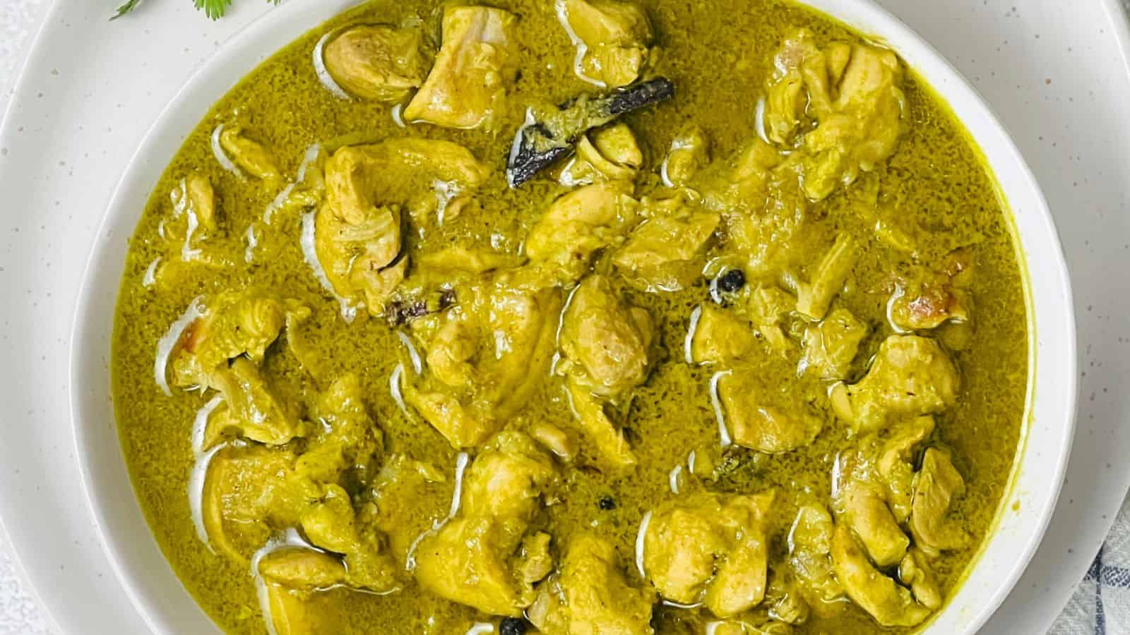 White bowl containing Dhaniya Chicken with a creamy, green sauce and garnished with herbs.