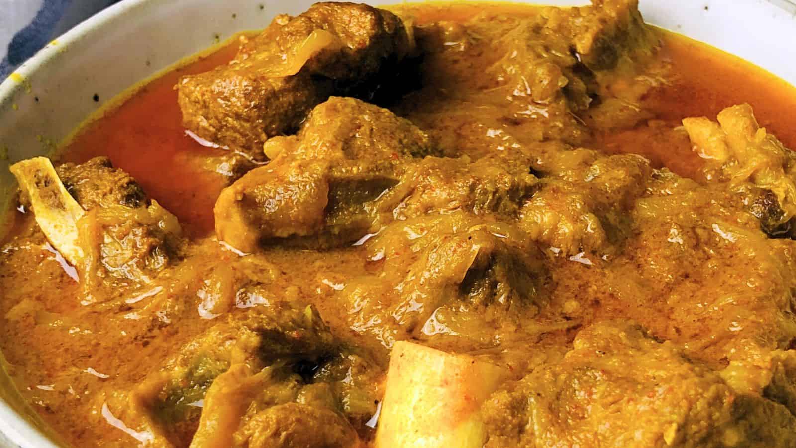 Bowl of Goat Curry with thick, rich gravy and chunks of meat on the bone.