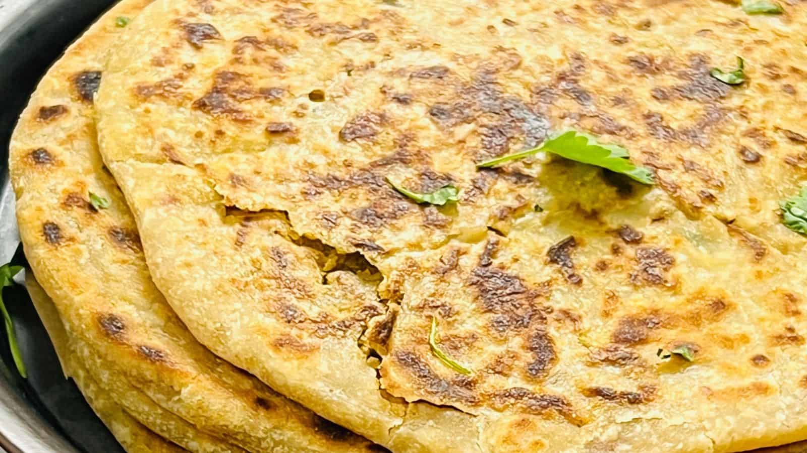 A stack of freshly cooked Gobi Paratha garnished with cilantro leaves on a black plate.