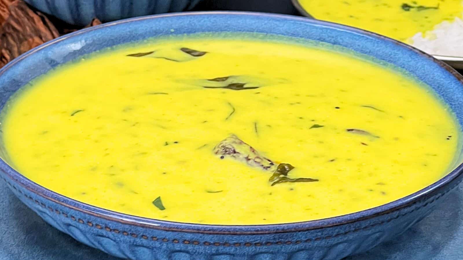 Bowl of creamy Gujarati Kadhi garnished with herbs, presented in a blue ceramic bowl.