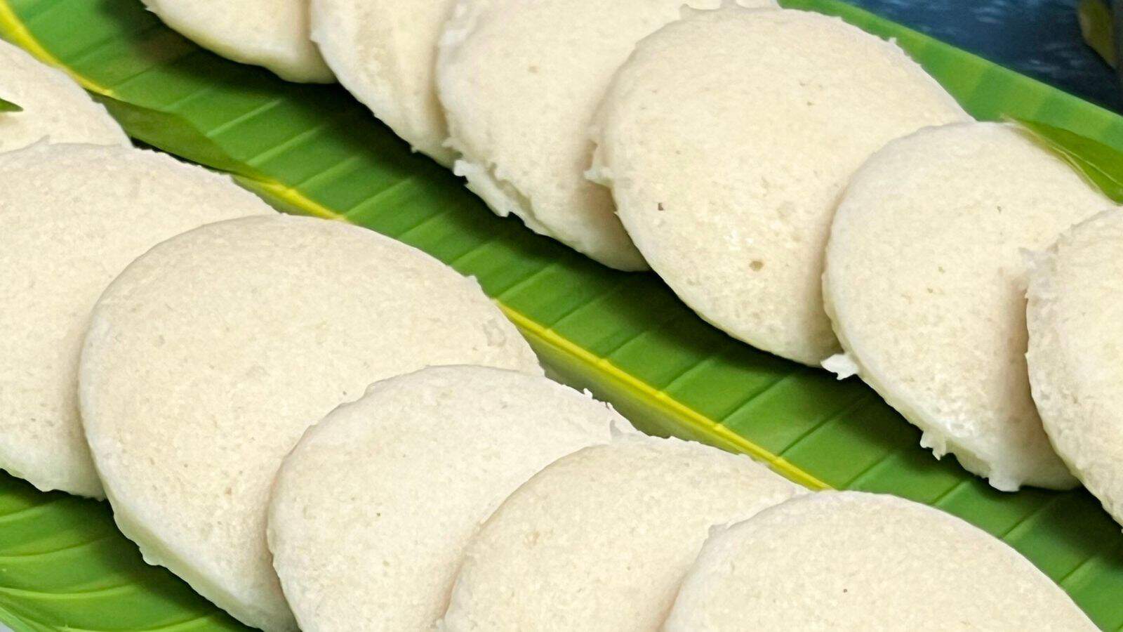 A row of idli, a traditional south indian steamed rice cake, served on a green banana leaf.