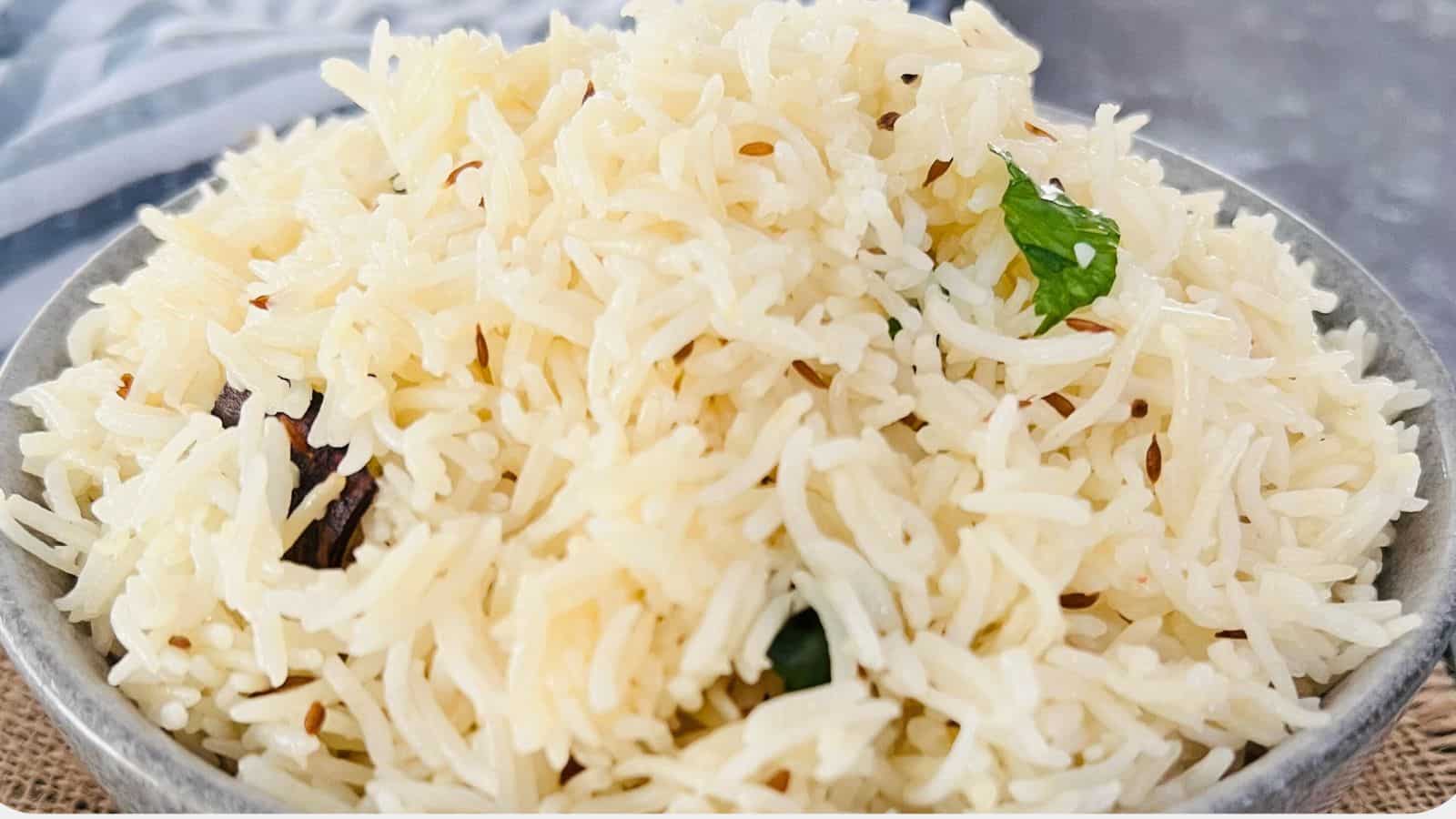 A bowl of cooked Jeera Rice, garnished, presented on a textured grey background.