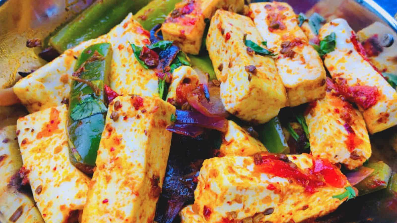 Kadai Paneer dish with slices of green bell peppers and red spices, garnished with herbs, served in a steel dish.