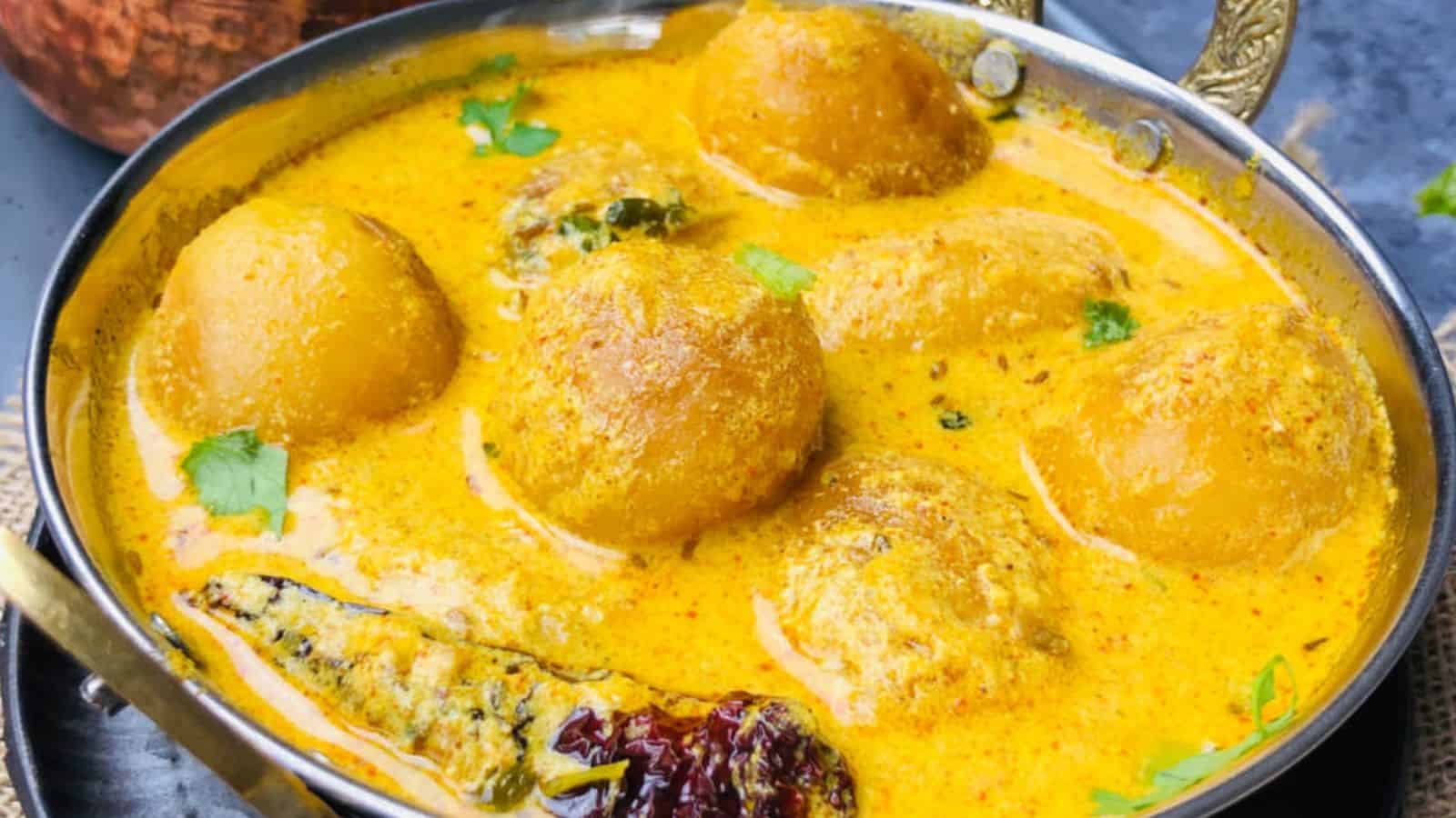 A bowl of Kashmiri Dum Aloo, a traditional Indian dish in a creamy yellow curry, garnished with fresh cilantro.