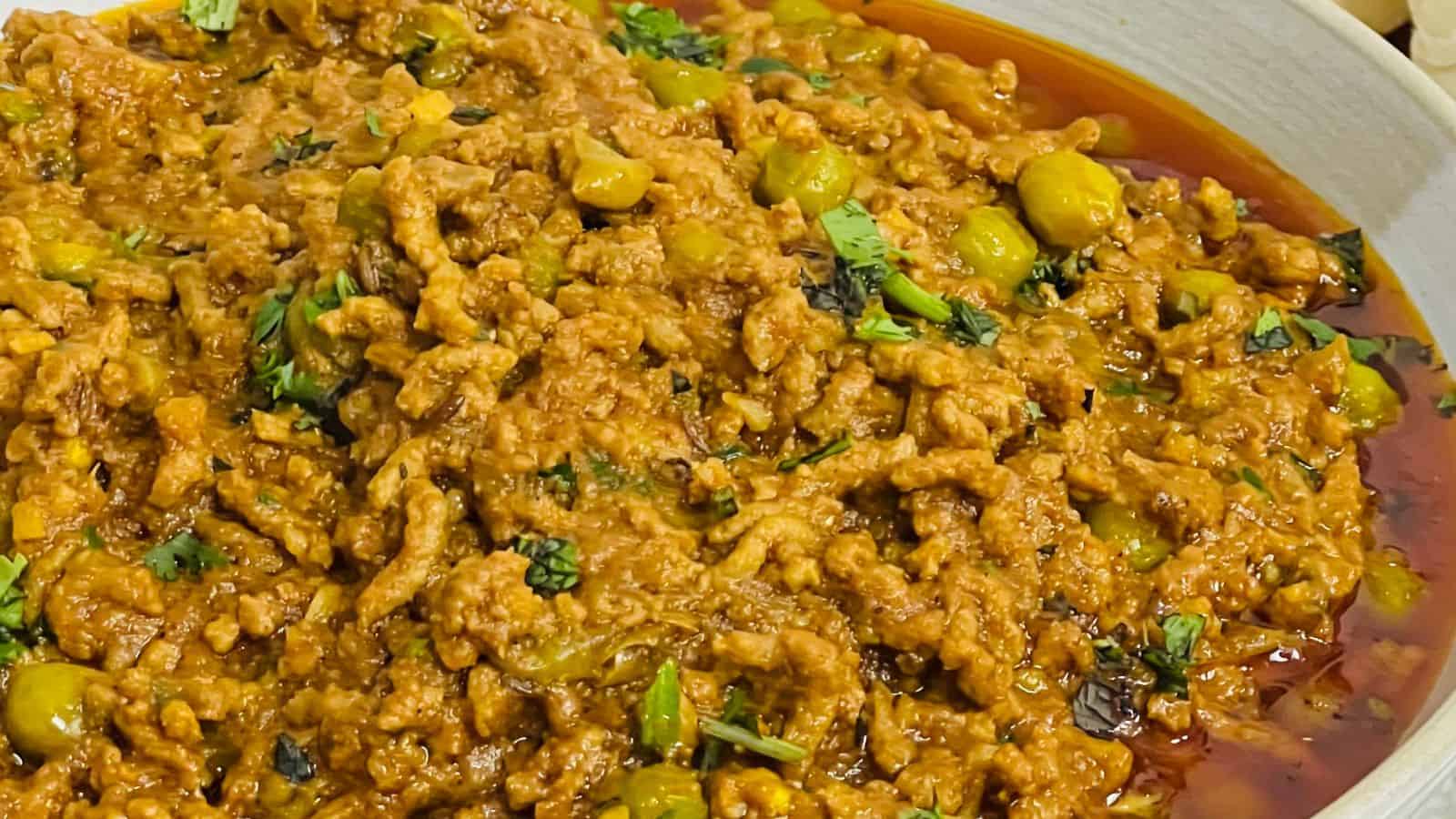 Close-up of cooked minced meat with green olives and chopped herbs in a sauce.