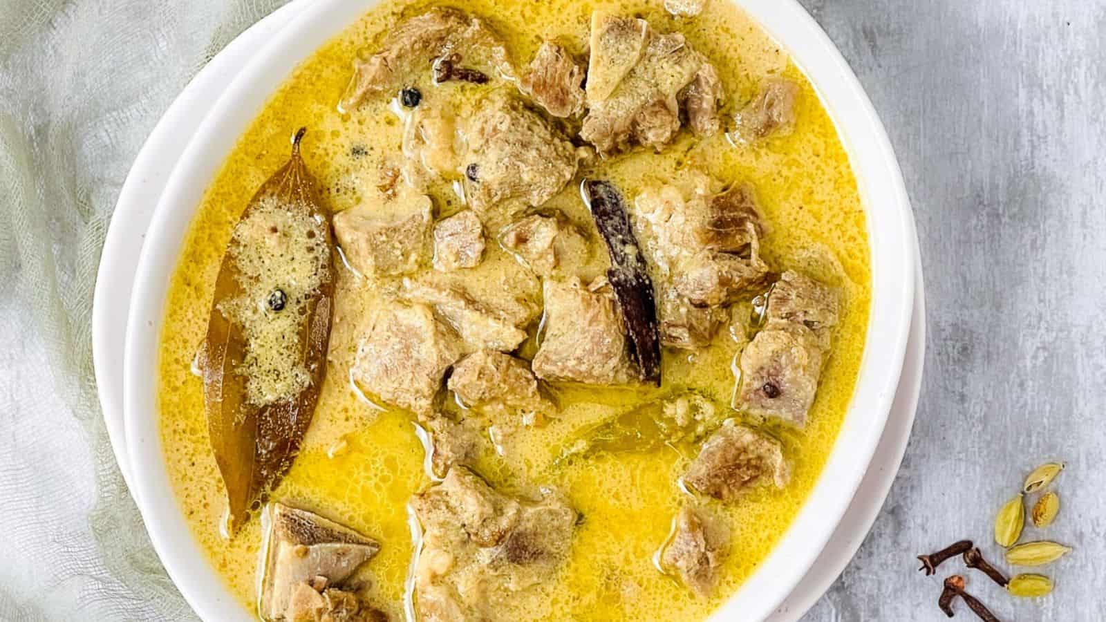 A bowl of traditional Lamb Rezala with spices and bay leaves, viewed from above.