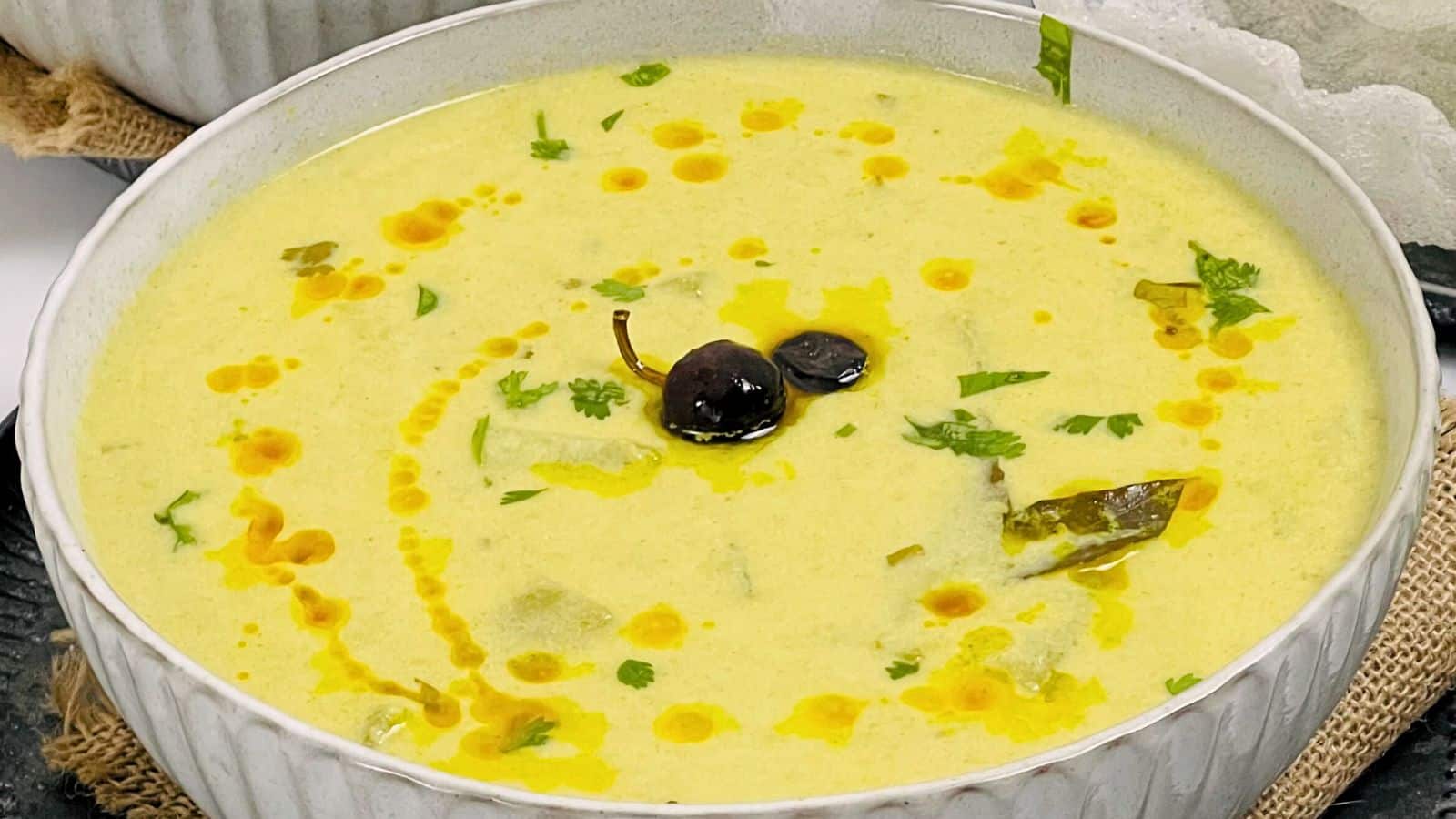 A bowl of creamy yellow soup garnished with herbs and oil on top of a cloth.