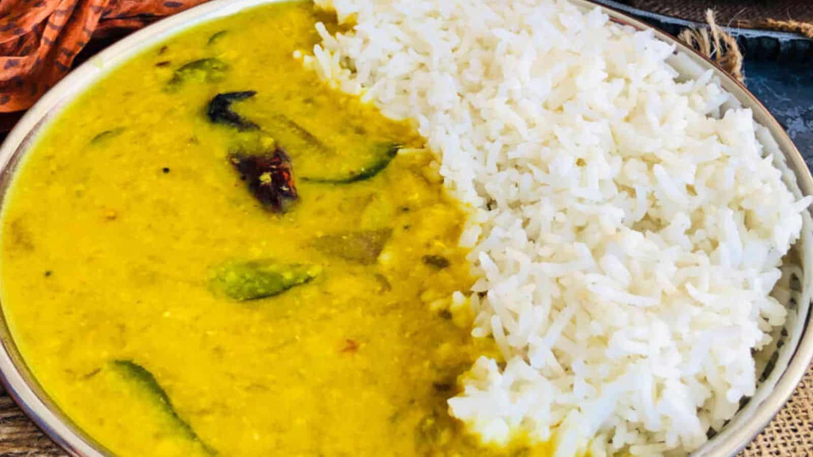 A plate of white rice paired with yellow dal garnished with chili peppers and curry leaves.