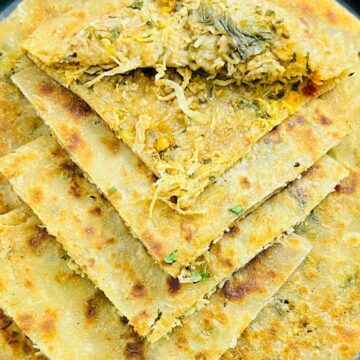 Close-up of stuffed parathas on a stovetop, filled with spiced vegetables, garnished with cilantro, cooked to a golden crisp.