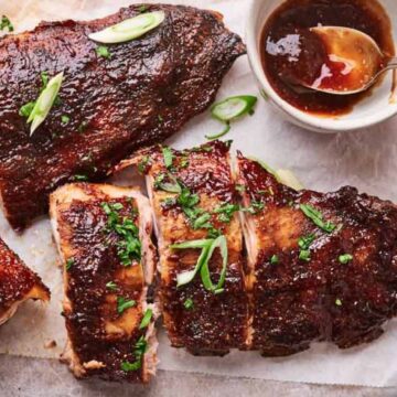 Grilled ribs garnished with herbs and served with a side of sauce and onions.