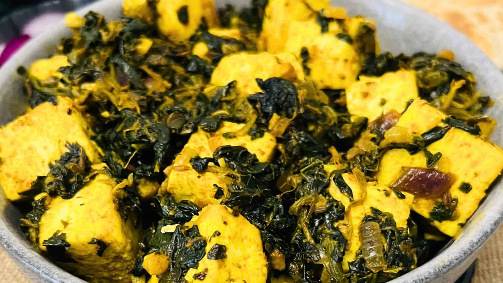 A bowl of indian Palak Paneer Stir Fry, featuring cubes of paneer cheese mixed with spiced, cooked spinach and herbs.