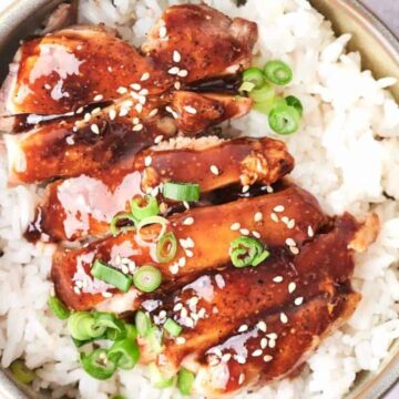 A bowl of white rice topped with glazed chicken and garnished with green onions and sesame seeds.